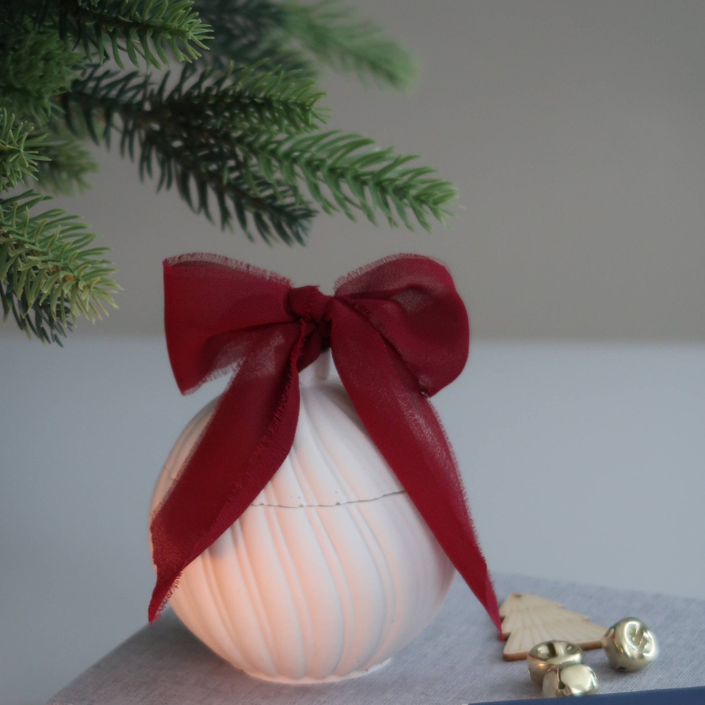 Decorative item with a red bow on a surface next to a book and small box.