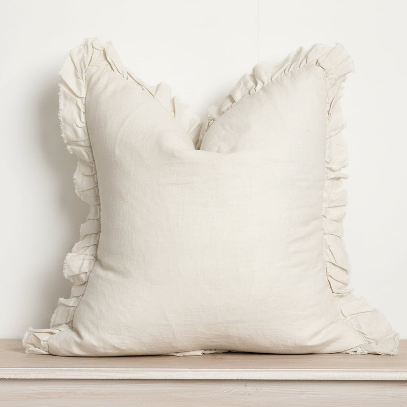 Beige pillow with ruffled edges on a wooden surface against a white background