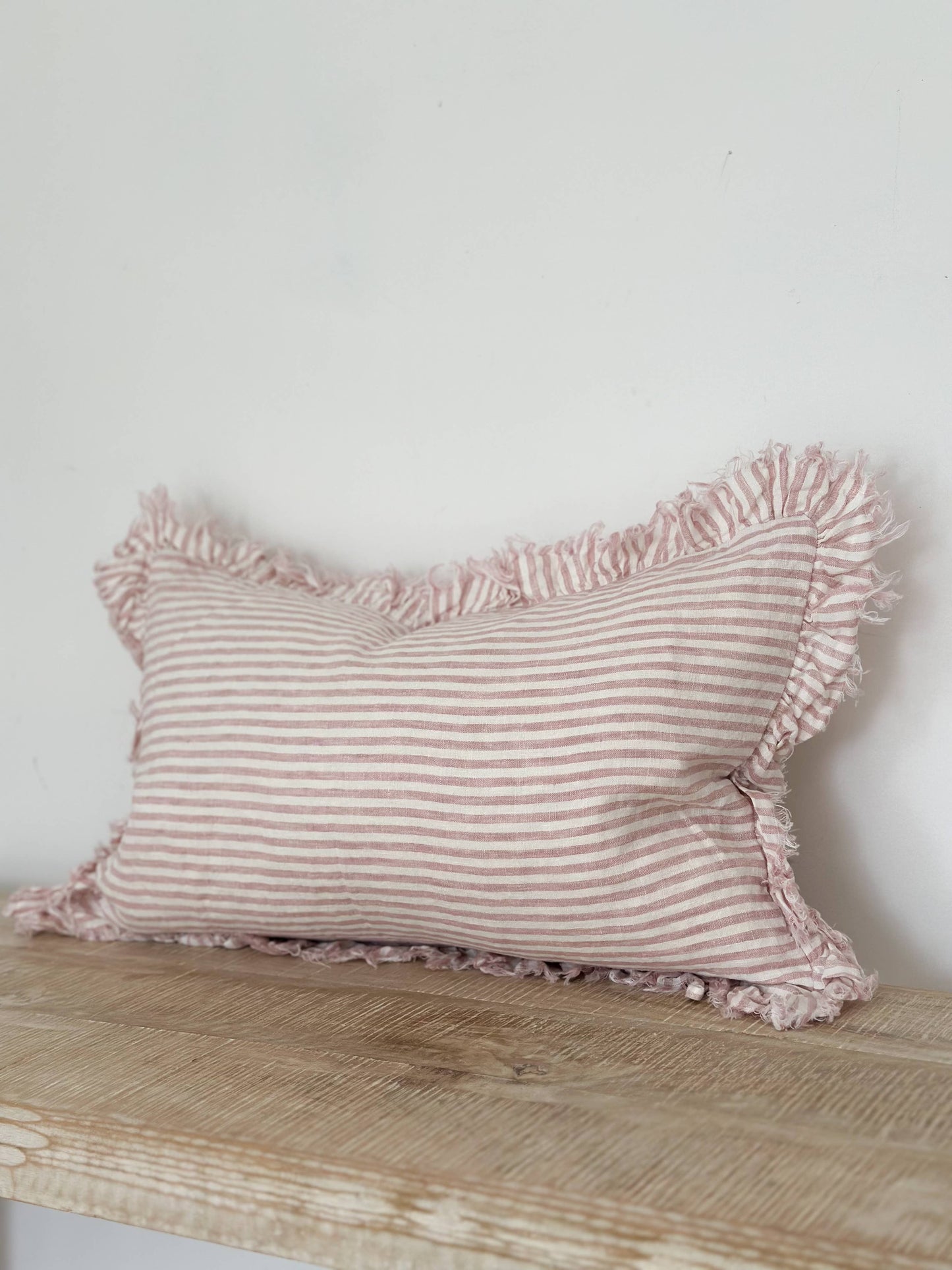 Pink striped pillow with ruffles on a wooden surface against a white wall