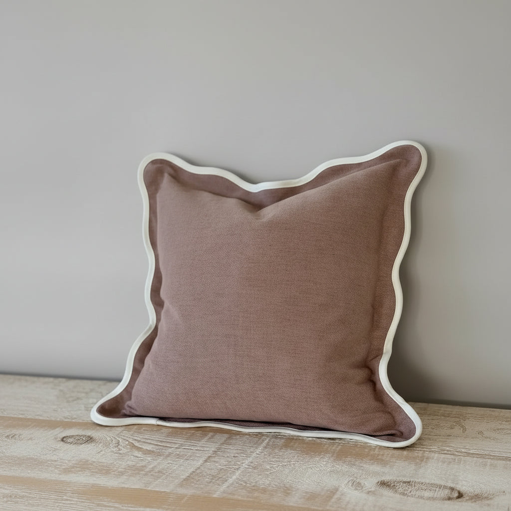 A large 65cm square cushion in dusty pink with a wavy scalloped edge detail on a contemporary bed set.