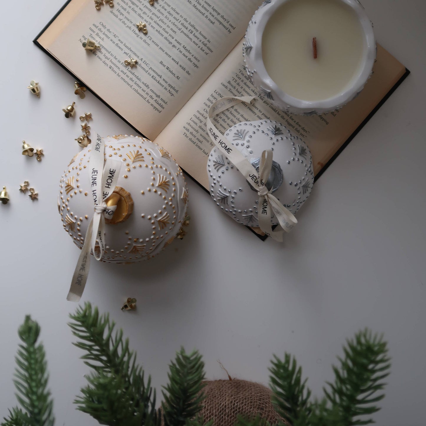 Decorative candles with gold accents on a white surface with an open book and greenery.