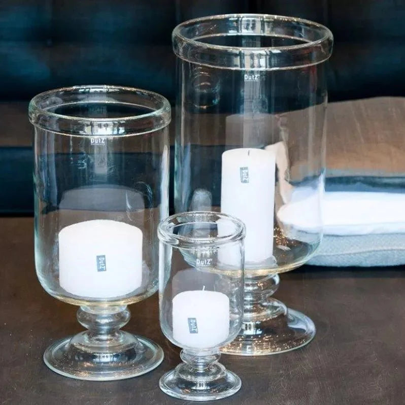 Set of glass candle holders with white candles on a wooden surface.