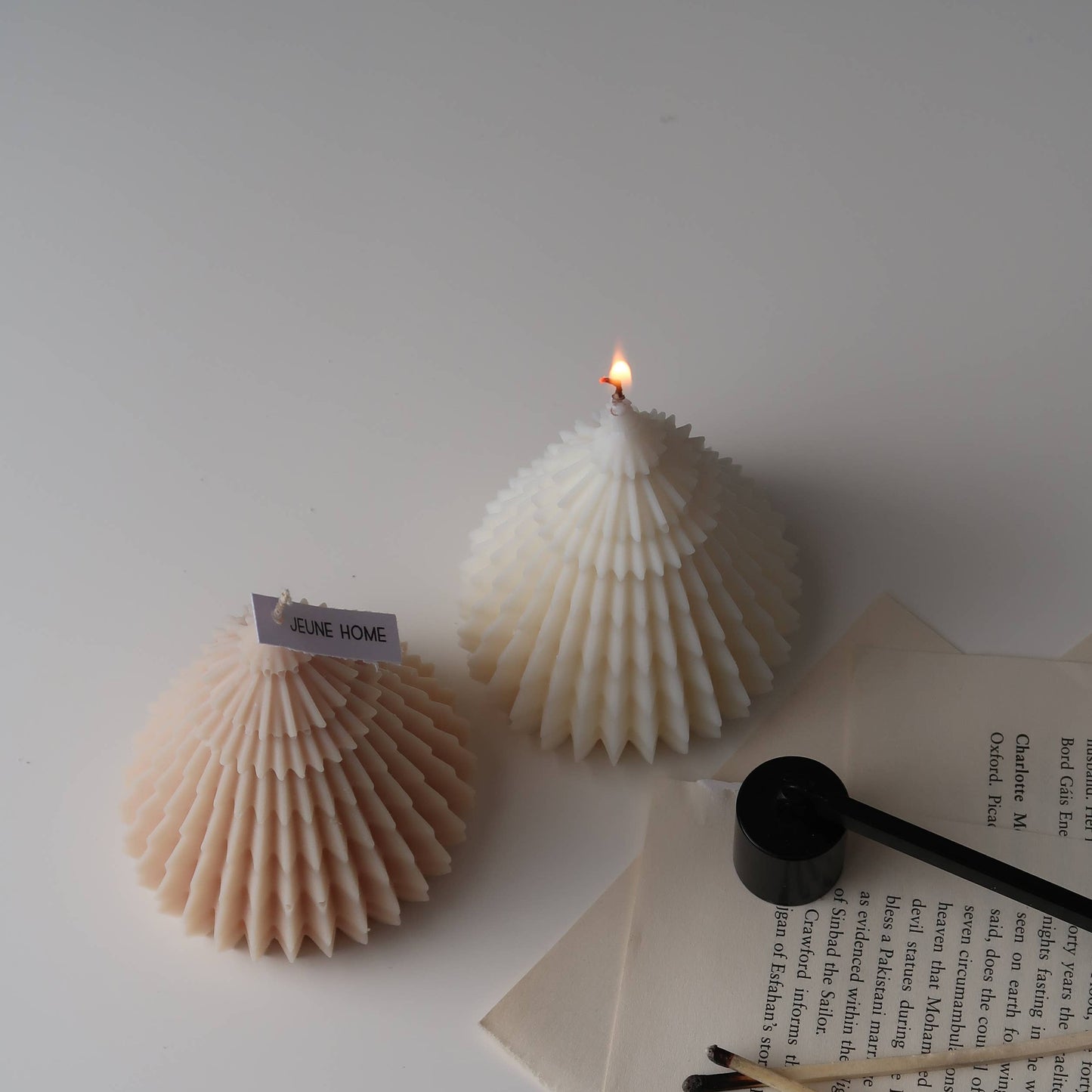 Two shell-shaped candles on a white surface with a book and pen.
