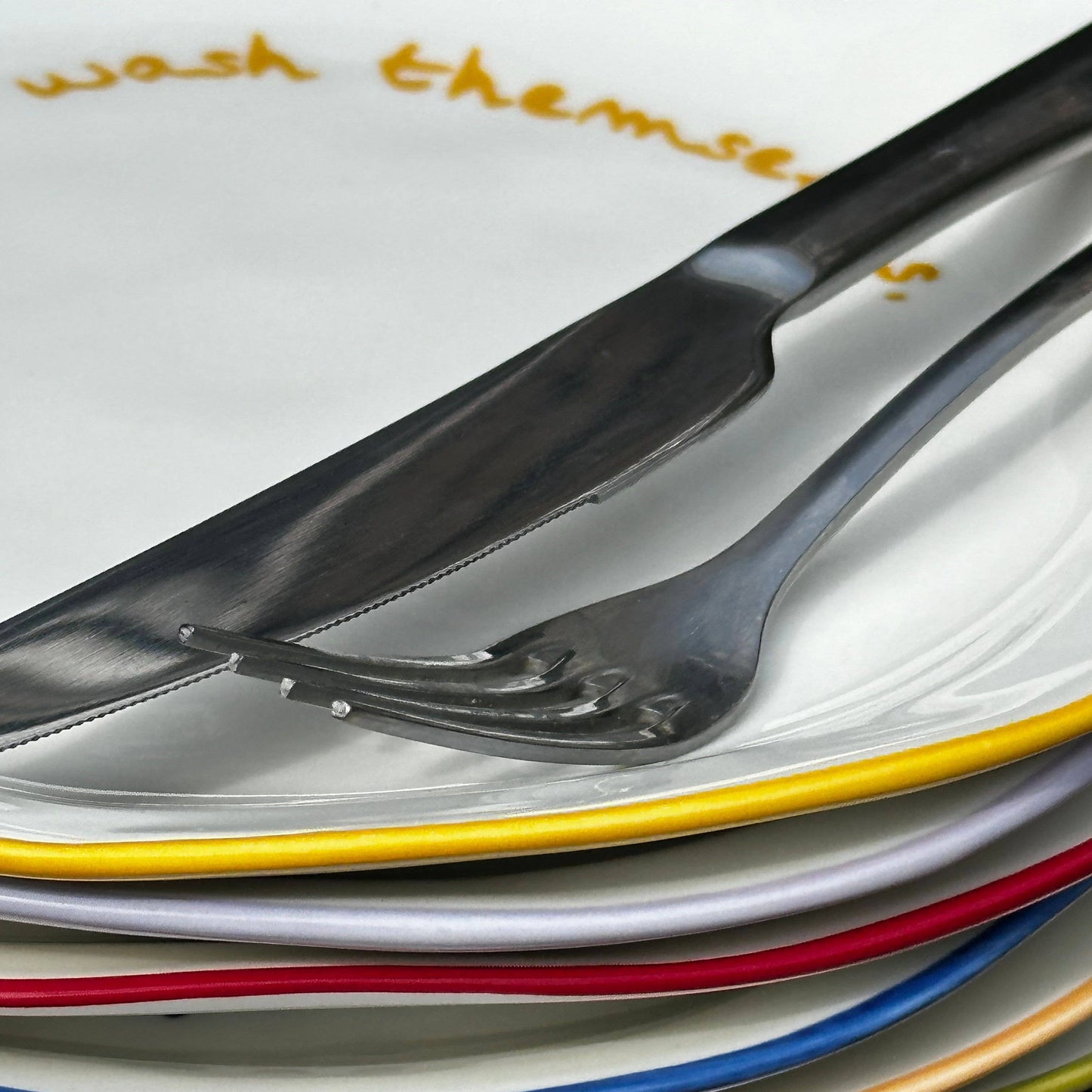 Stack of colorful plates with cutlery on a wooden surface