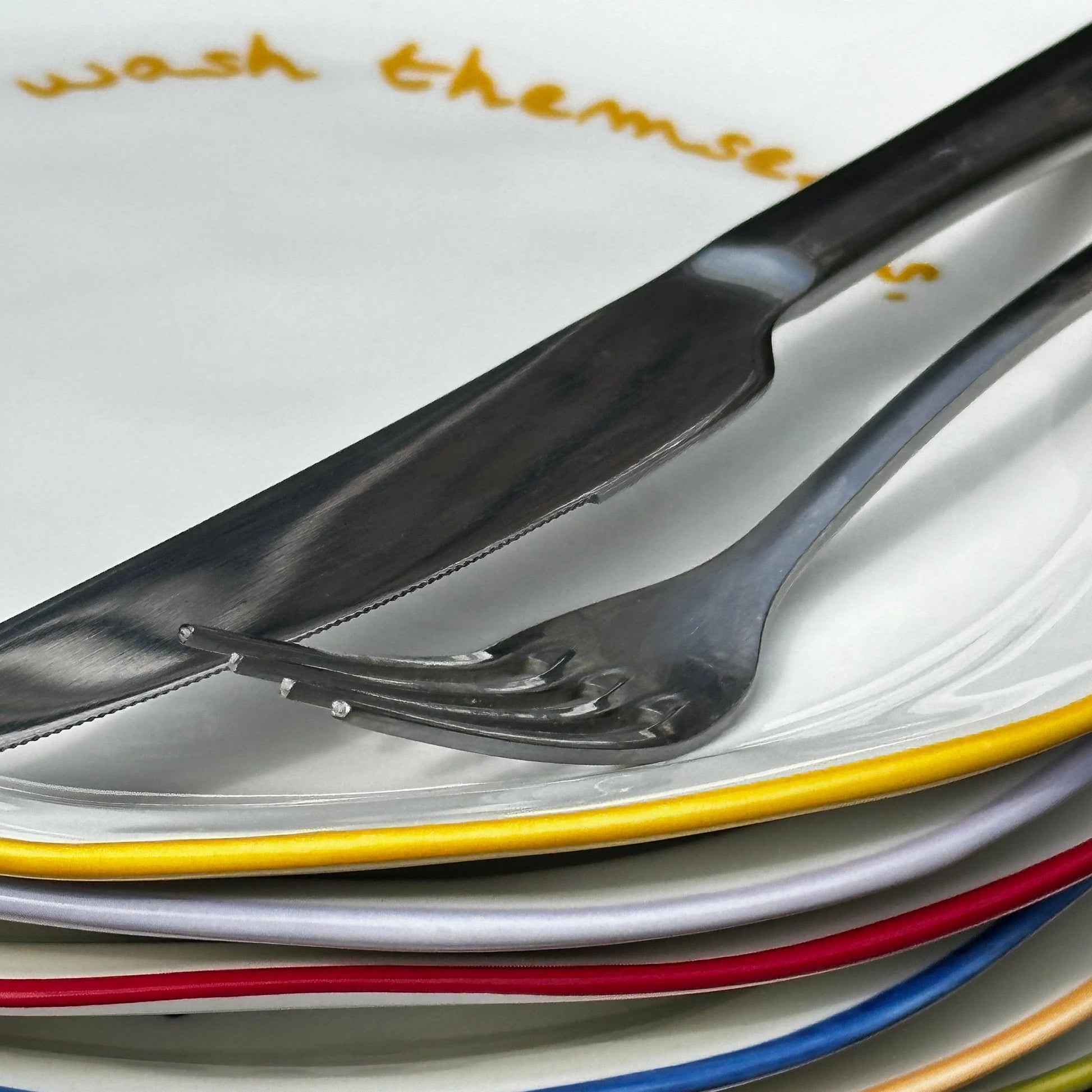 Stack of colorful plates with cutlery on a wooden surface
