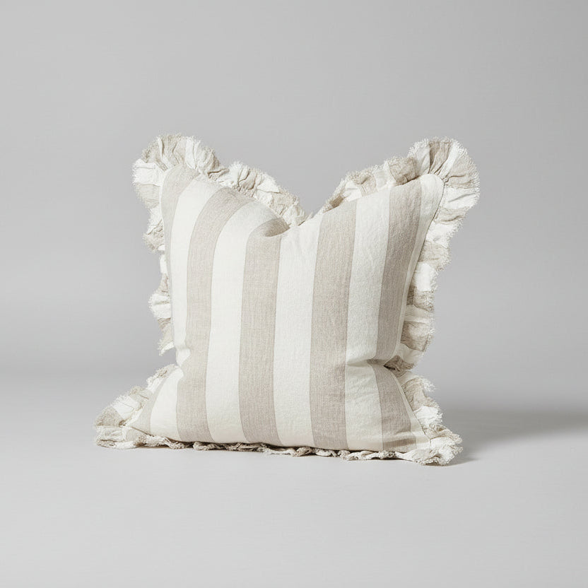 Striped pillow with ruffled edges on a wooden surface against a light background