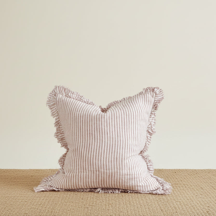 Pink striped pillow with ruffled edges on a wooden surface against a light gray background