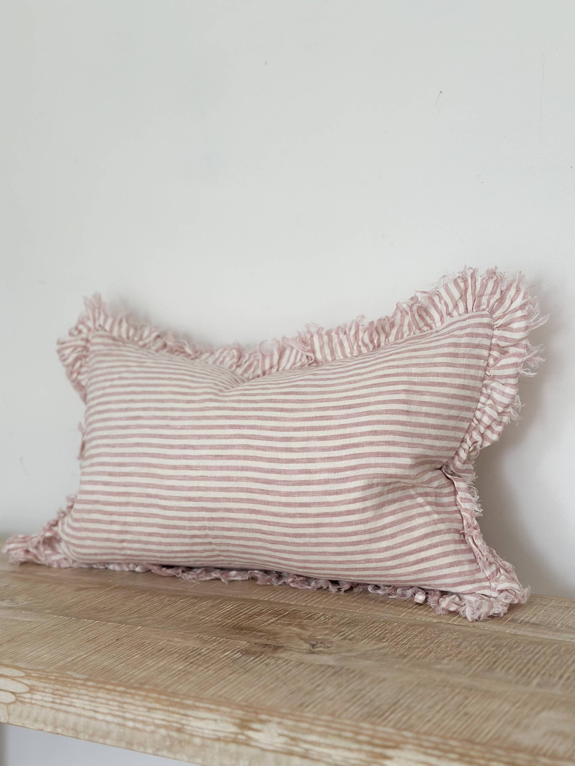 Pink striped pillow with ruffles on a wooden surface against a white wall