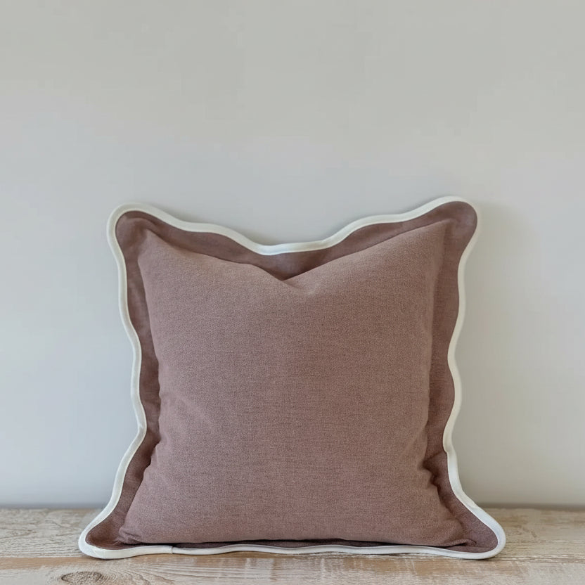 A large 65cm square cushion in dusty pink with a wavy scalloped edge detail on a contemporary bed set.