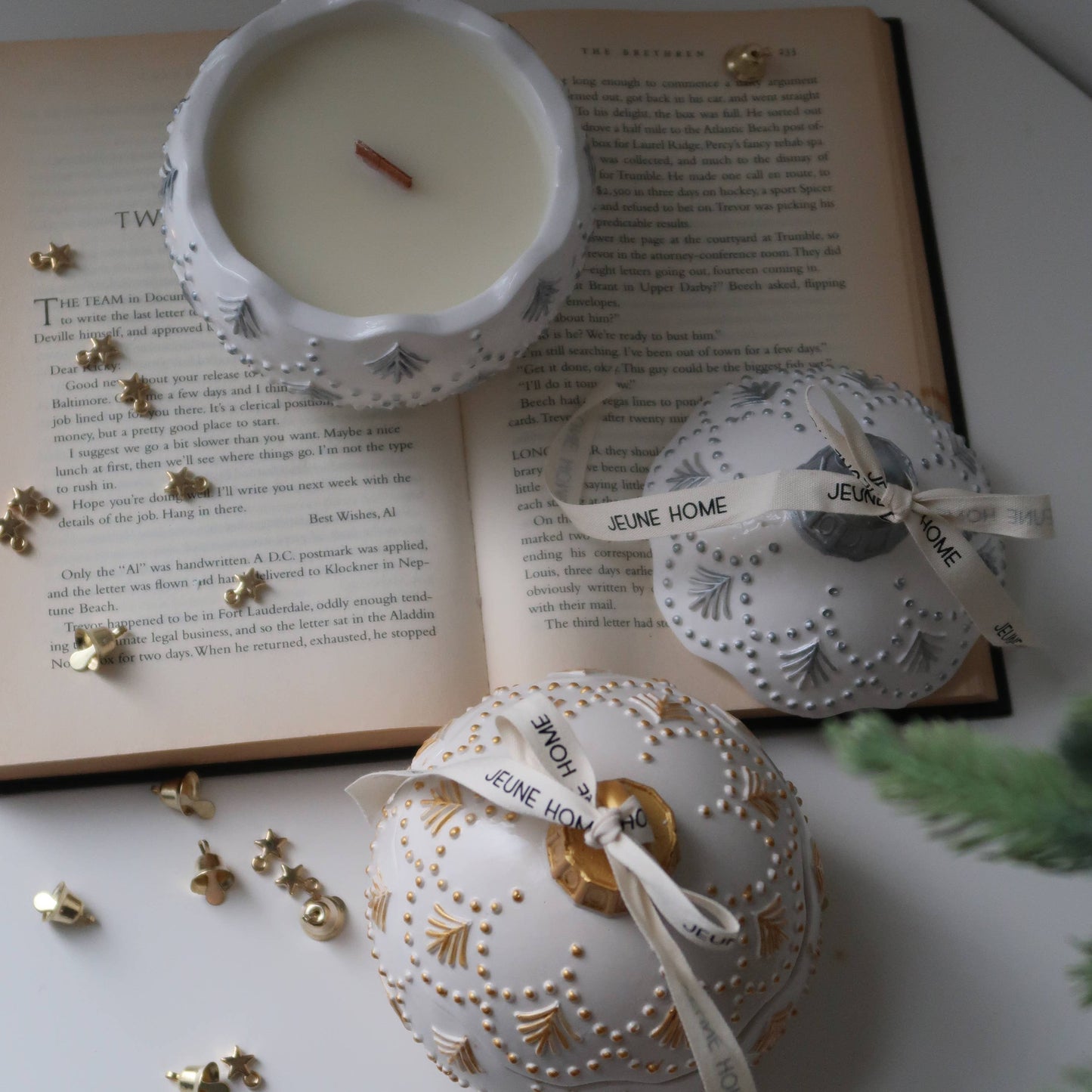 Decorative white ornaments with gold accents on a surface with an open book and small candle.