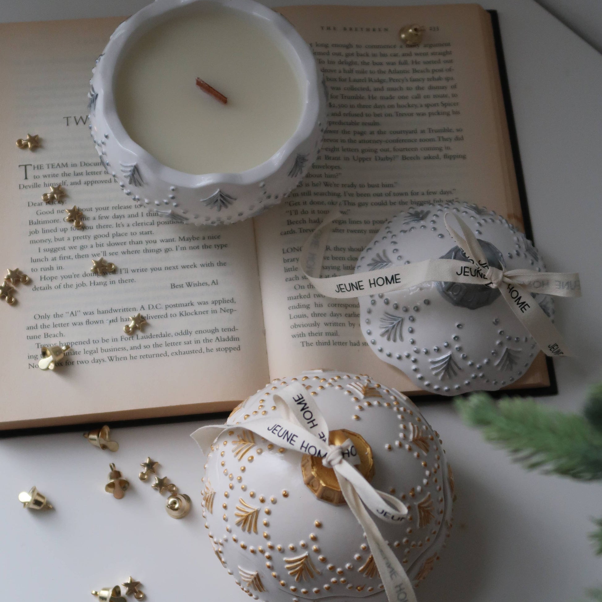 Decorative white ornaments with gold accents on a surface with an open book and small candle.