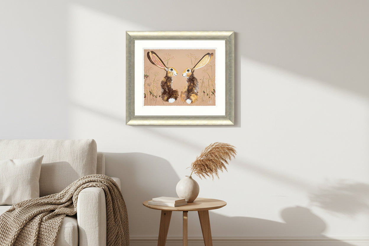Framed pastel artwork of two long-eared brown hares facing each other amid delicate wildflowers.