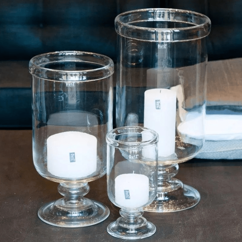 Set of clear glass candle holders with white candles on a dark surface