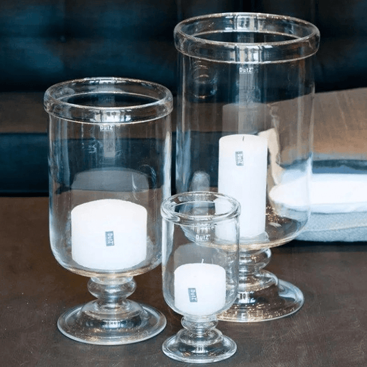 Set of clear glass candle holders with white candles on a dark surface