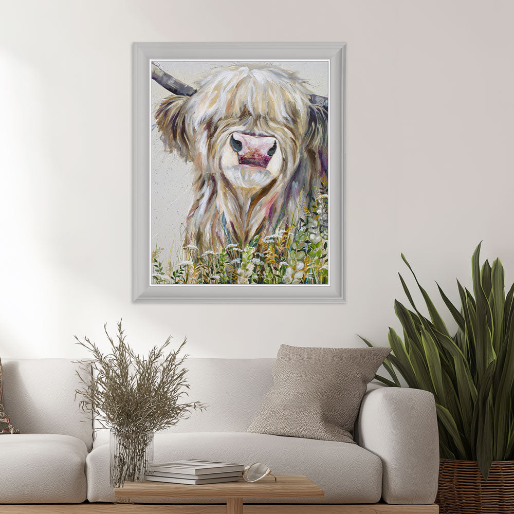 Framed artwork of a highland cow in a living room setting with a sofa and plants.