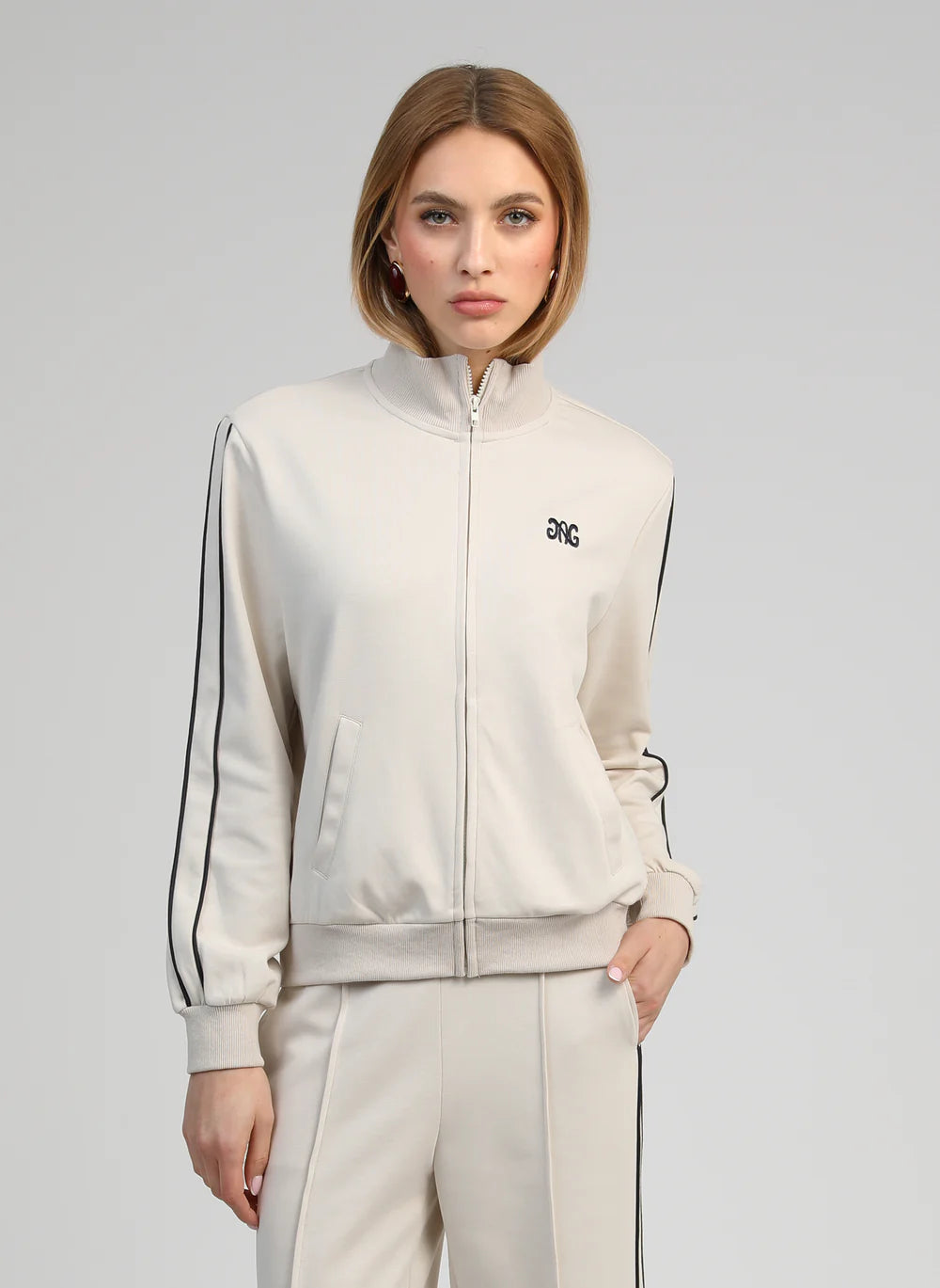 Woman wearing a light gray tracksuit with black stripes on a gray background