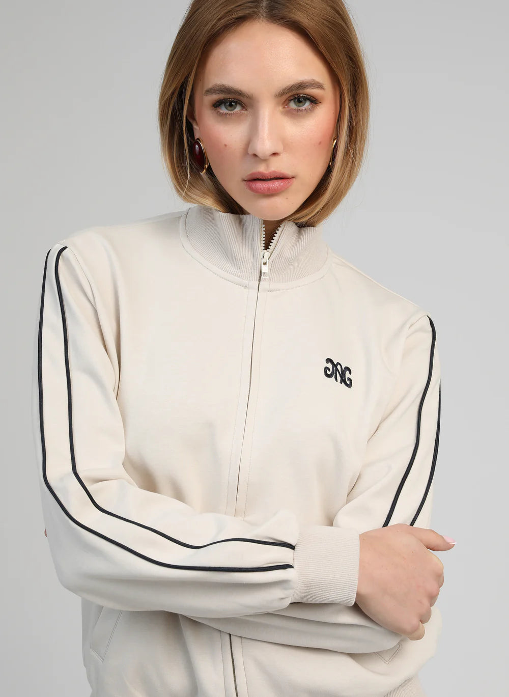 Woman wearing a cream-colored tracksuit with black stripes on a gray background