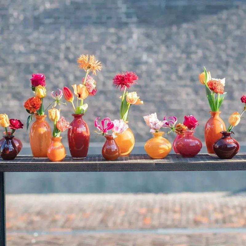 Row of colorful vases with flowers on a table outdoors.