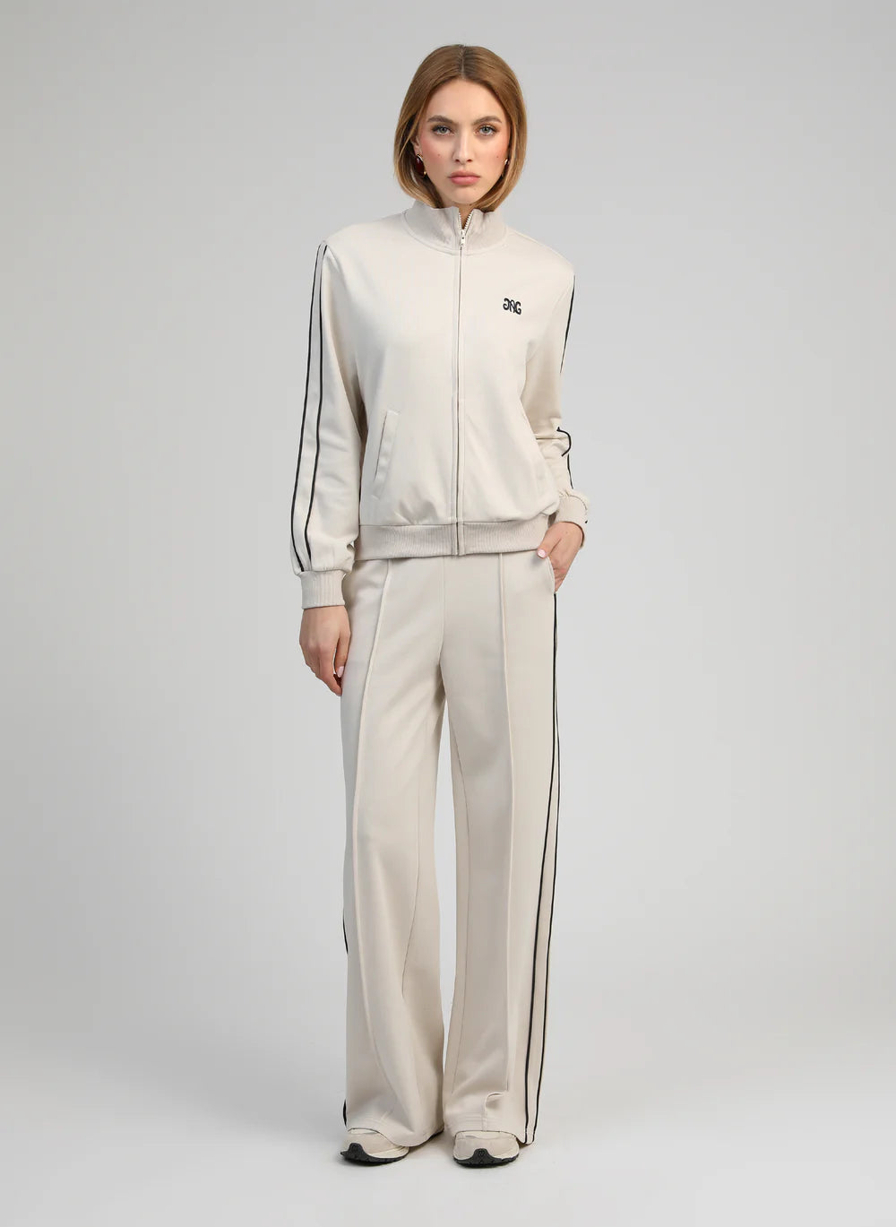 Woman wearing a beige tracksuit with black stripes on a light gray background
