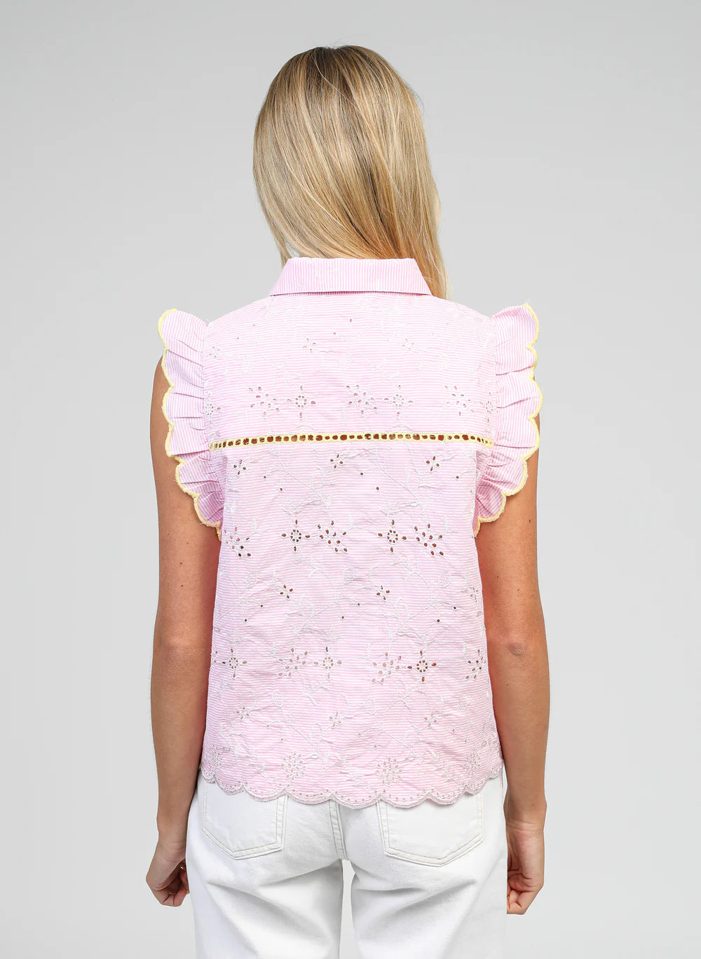 Woman wearing a pink embroidered top with ruffled sleeves on a gray background