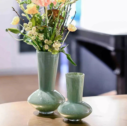 Two green vases on a table with one containing flowers.
