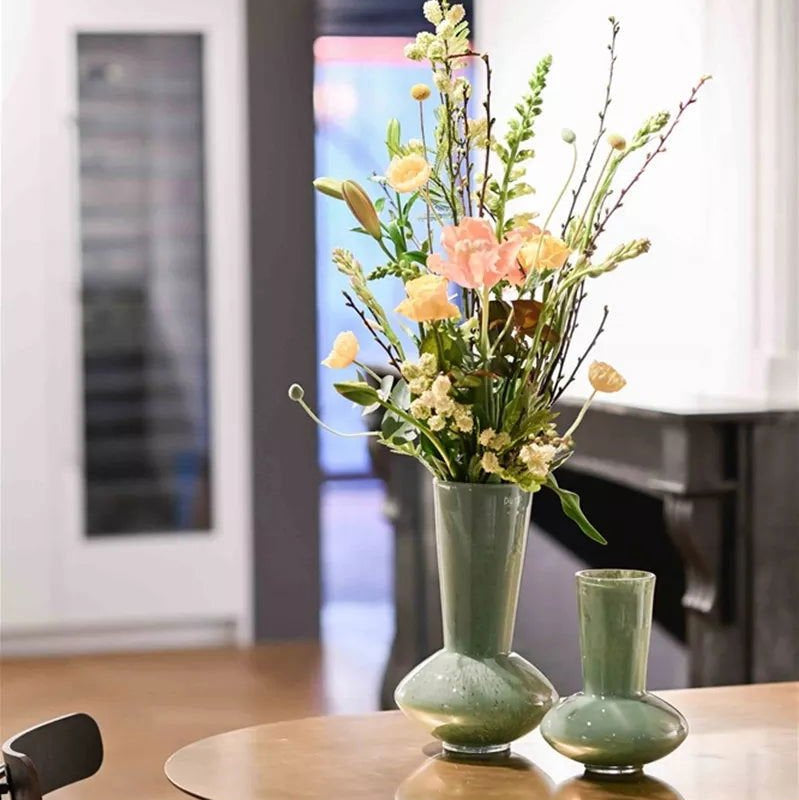 Two green vases with flowers on a table in a room with a blurred background