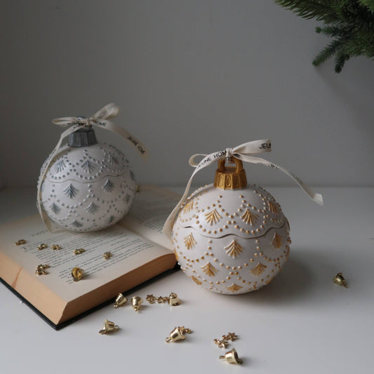 Decorative Christmas ornaments with gold accents on a white surface next to an open book and small tree.