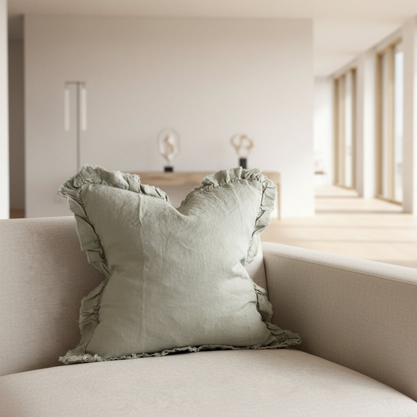 A square 53cm Dusty Sage linen cushion with a ruffled edge, styled on a neutral-toned armchair.