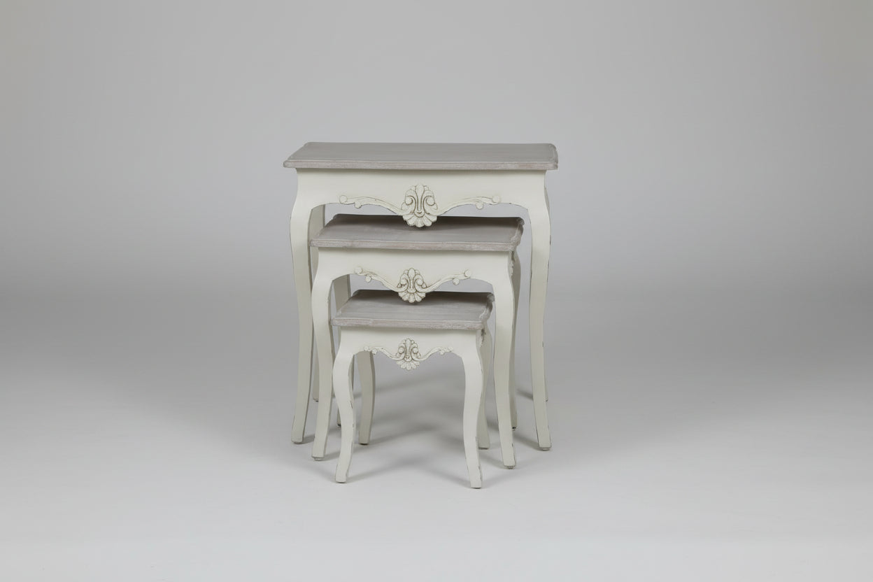 Set of three Nesting tables with decorative carvings on a beige rug.