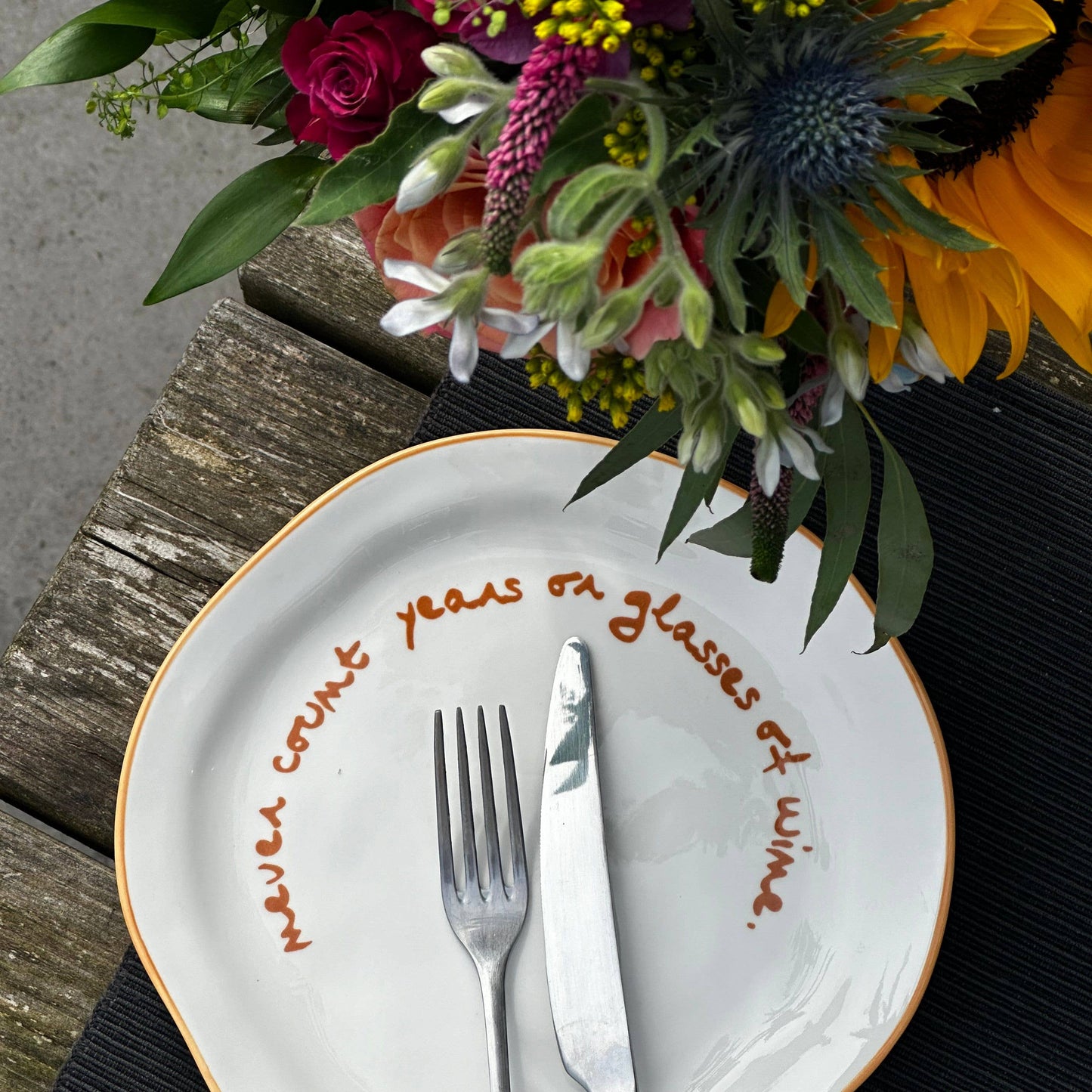 Floral arrangement with a decorative plate featuring text on a wooden surface