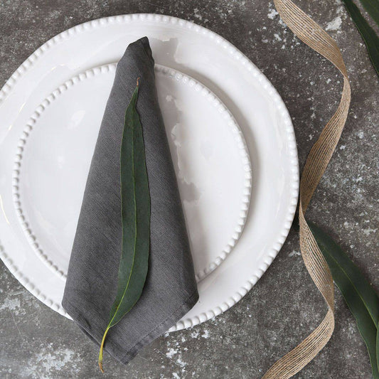 White plates and a gray napkin with a green leaf on a textured gray surface, beige ribbon beside.