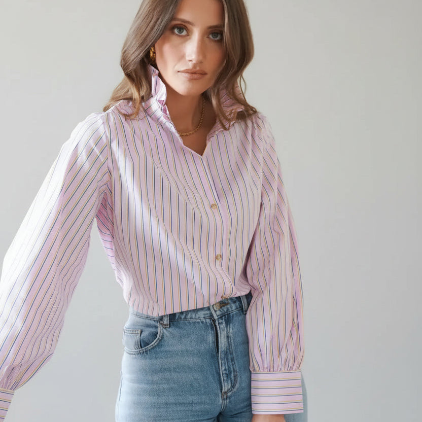 Woman wearing a pink striped shirt and blue jeans indoors.