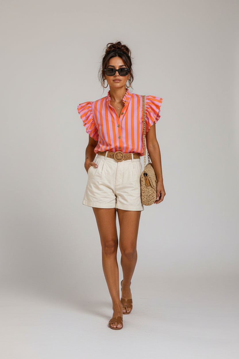 Woman walking on a street wearing a striped shirt and shorts, with a cafe in the background.