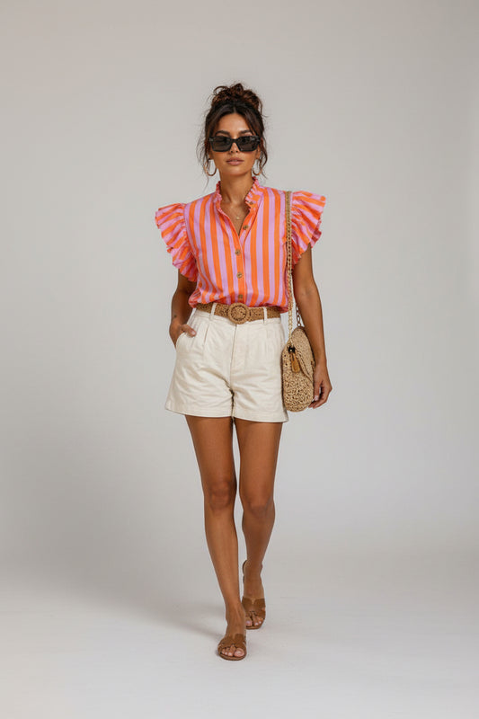 Woman walking on a street wearing a striped shirt and shorts, with a cafe in the background.