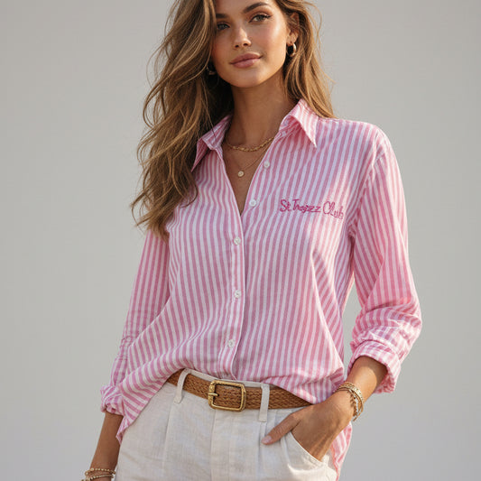 Woman wearing a pink and white striped shirt with 'St. Tropez' logo by a waterfront.