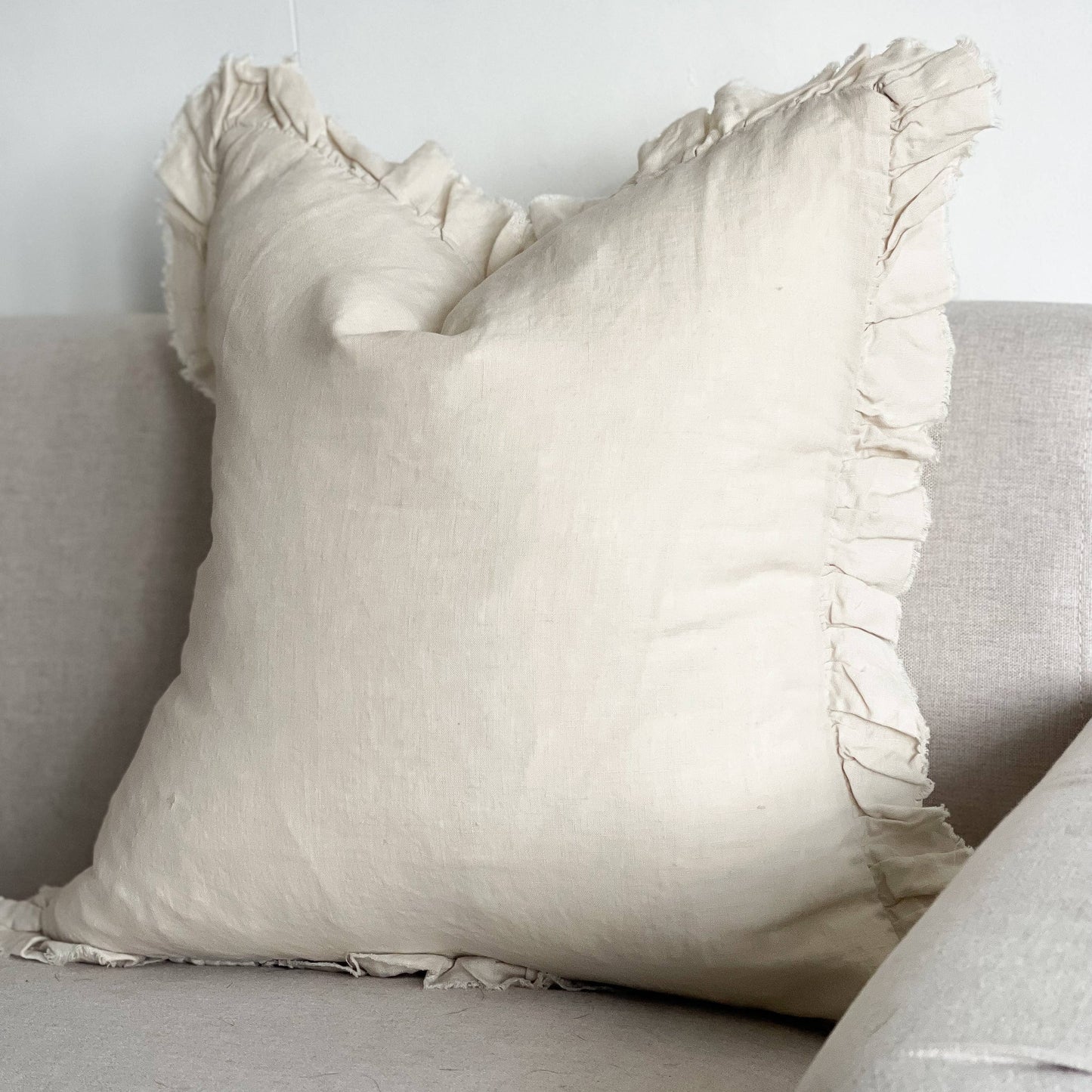 Beige pillow with ruffled edges on a light gray sofa against a white wall