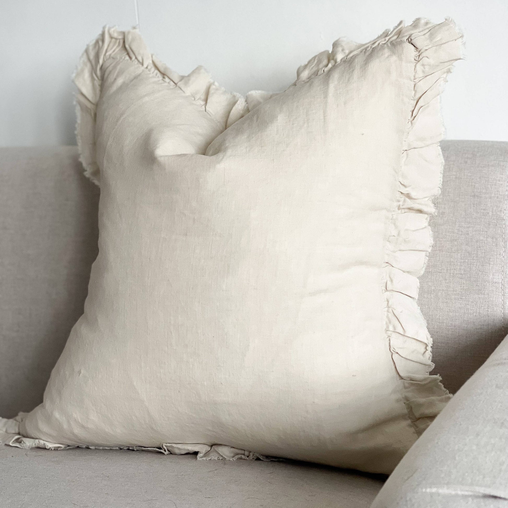 Beige pillow with ruffled edges on a light gray sofa against a white wall