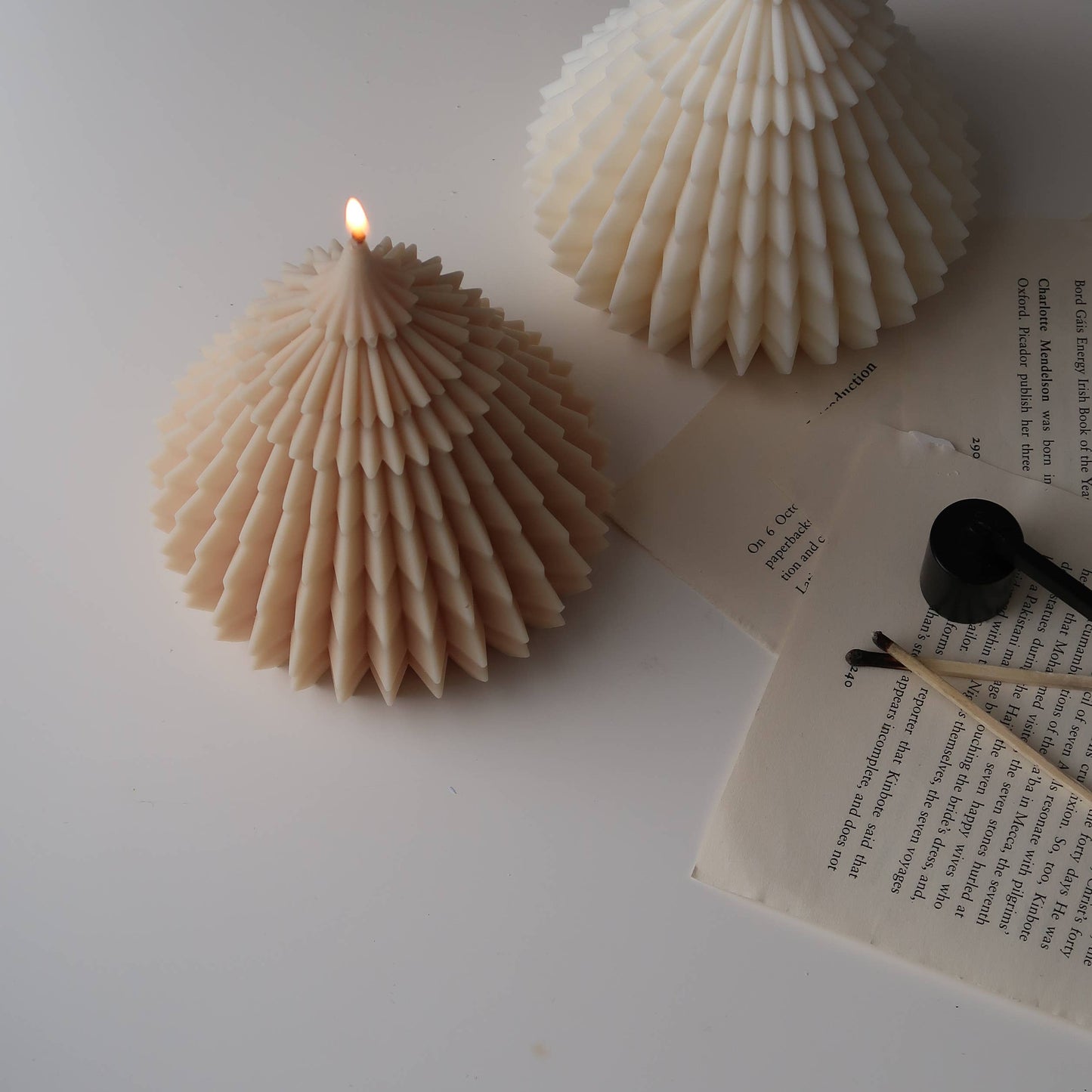 Two shell-shaped candles on a white surface with an open book.