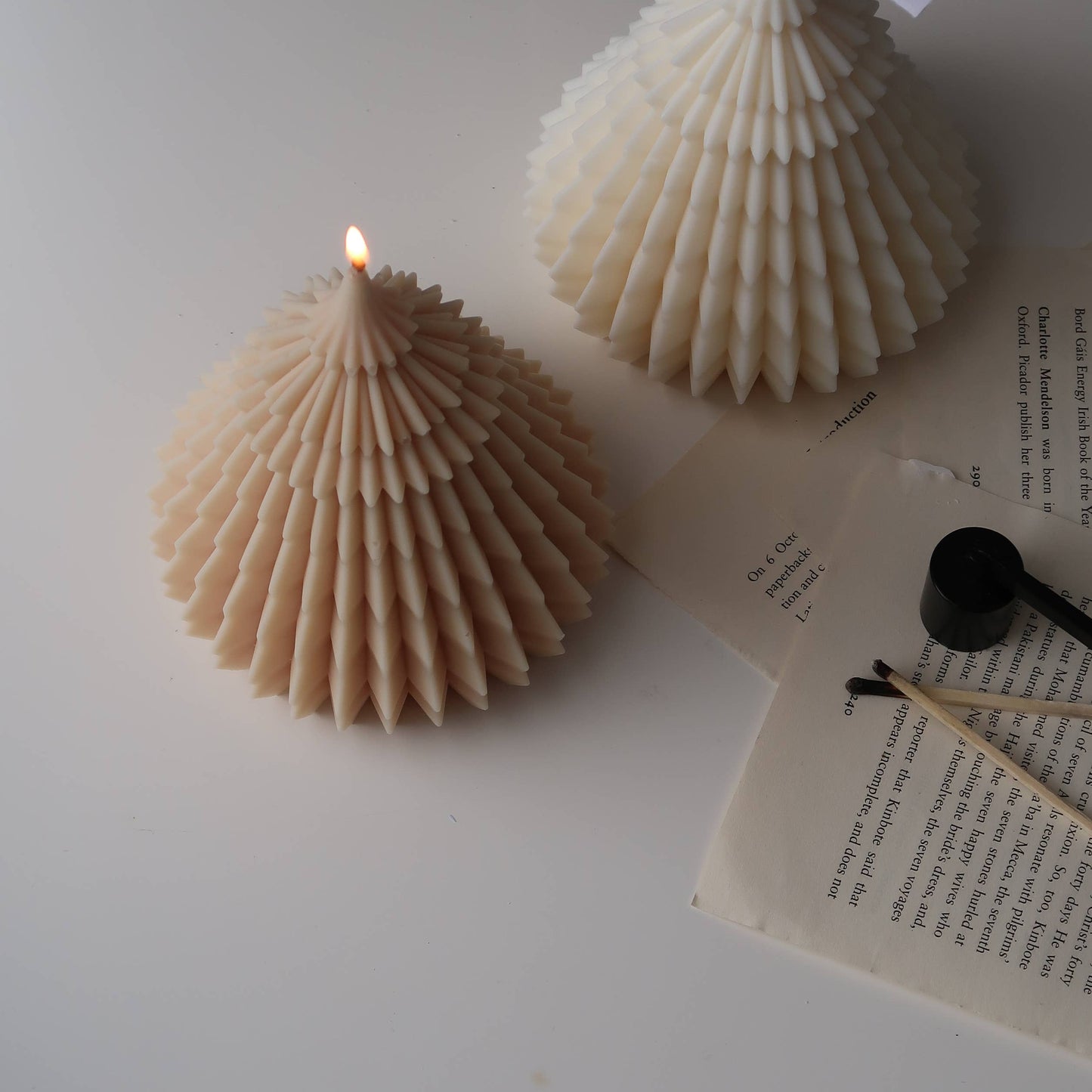 Two shell-shaped candles on a white surface with an open book.
