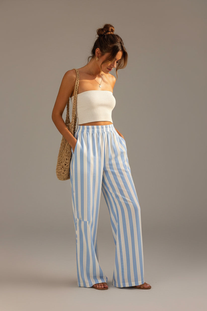 Woman wearing a white top and blue striped pants standing against a beige wall.