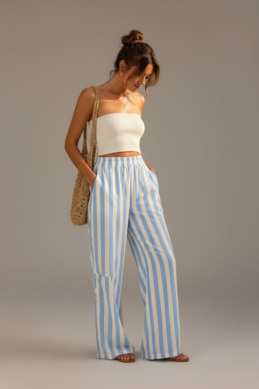 Woman wearing a white top and blue striped pants standing against a beige wall.