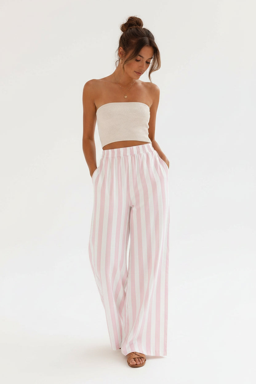 Woman wearing a white top and pink striped pants in a minimalistic setting.