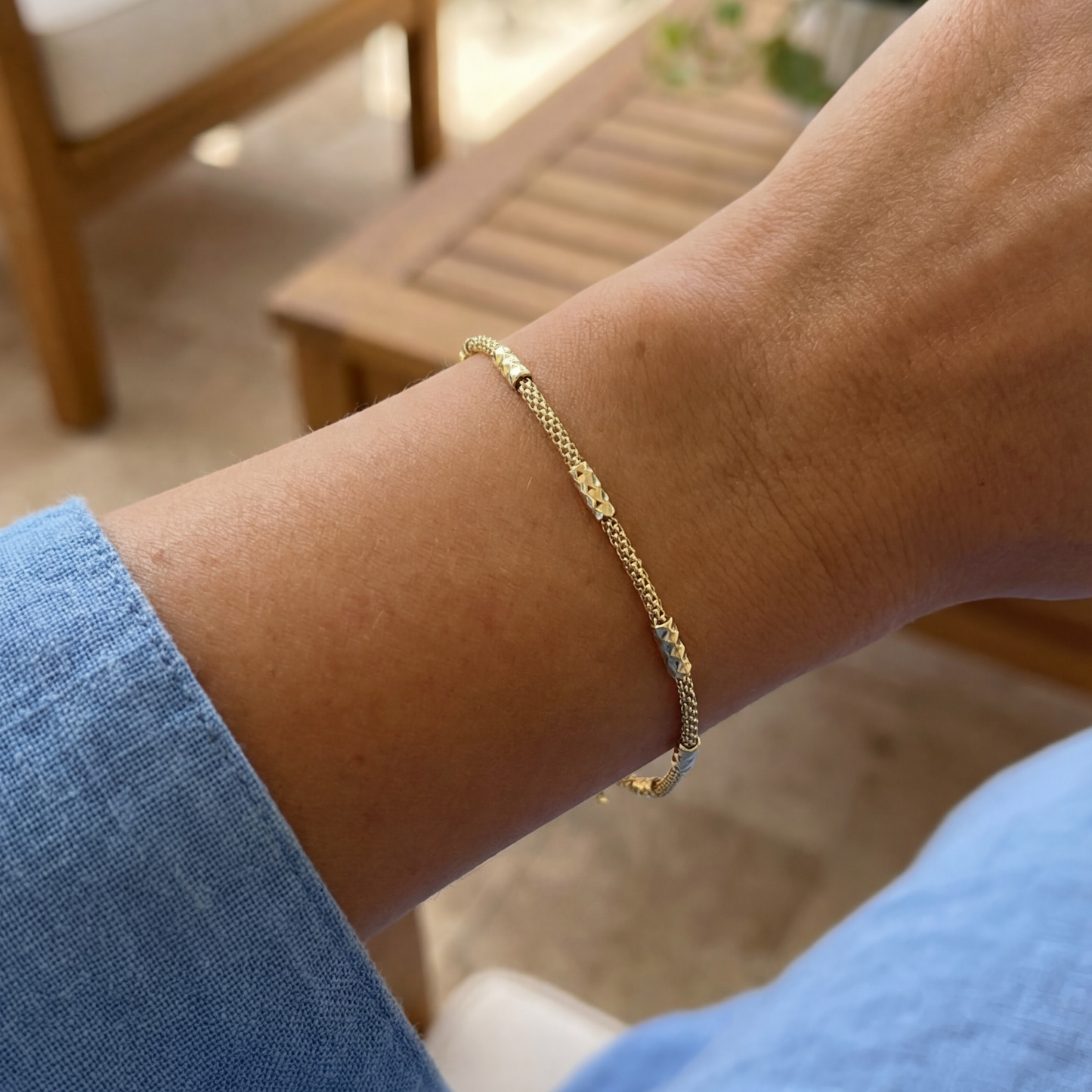 Gold bracelet on a wrist with a blurred outdoor background